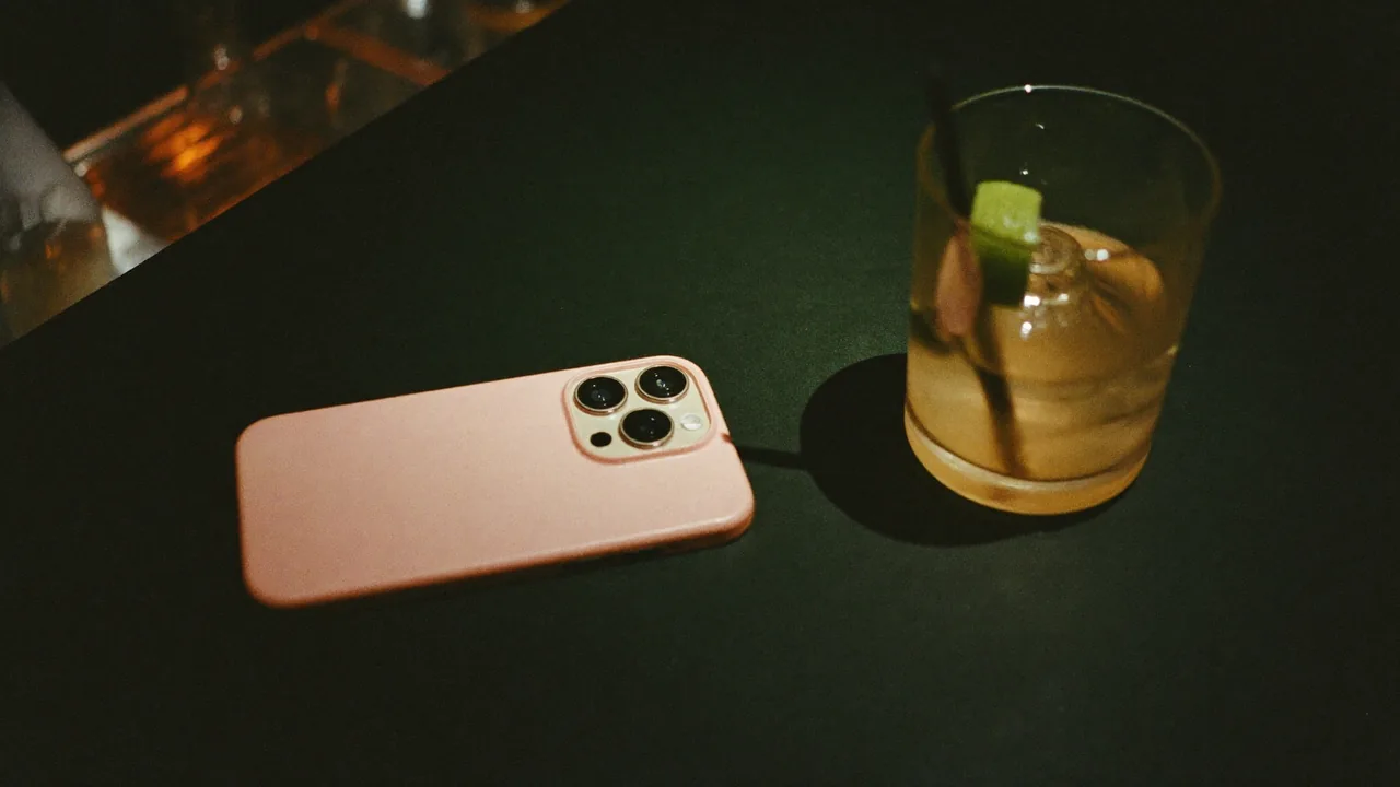 A phone face down on a dark bar counter beside a half finished drink