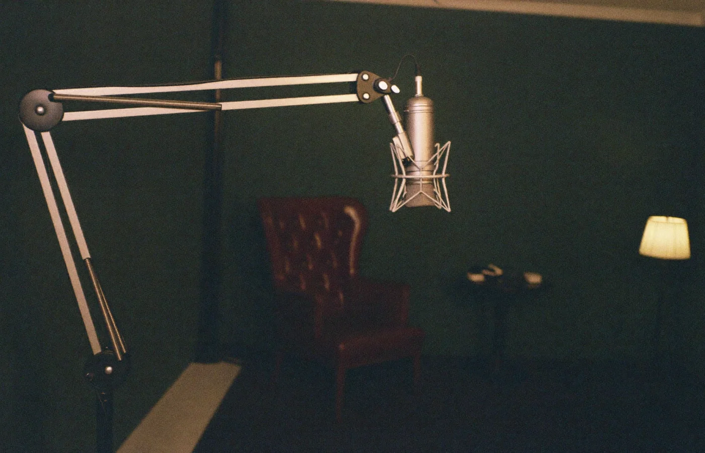 The recording setup at night: a studio microphone, a leather chair and one warm lamp against a dark green wall